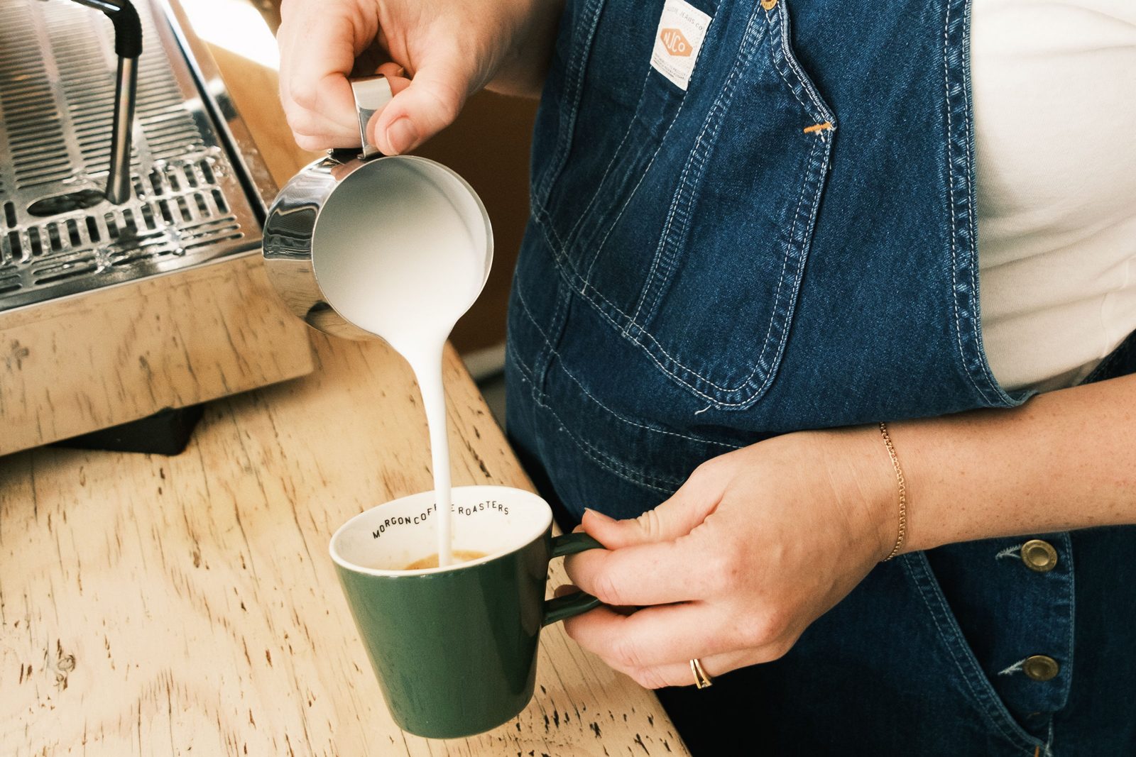 Milch wird aus einem Kännchen in eine grüne Tasse mit Espresso gegossen